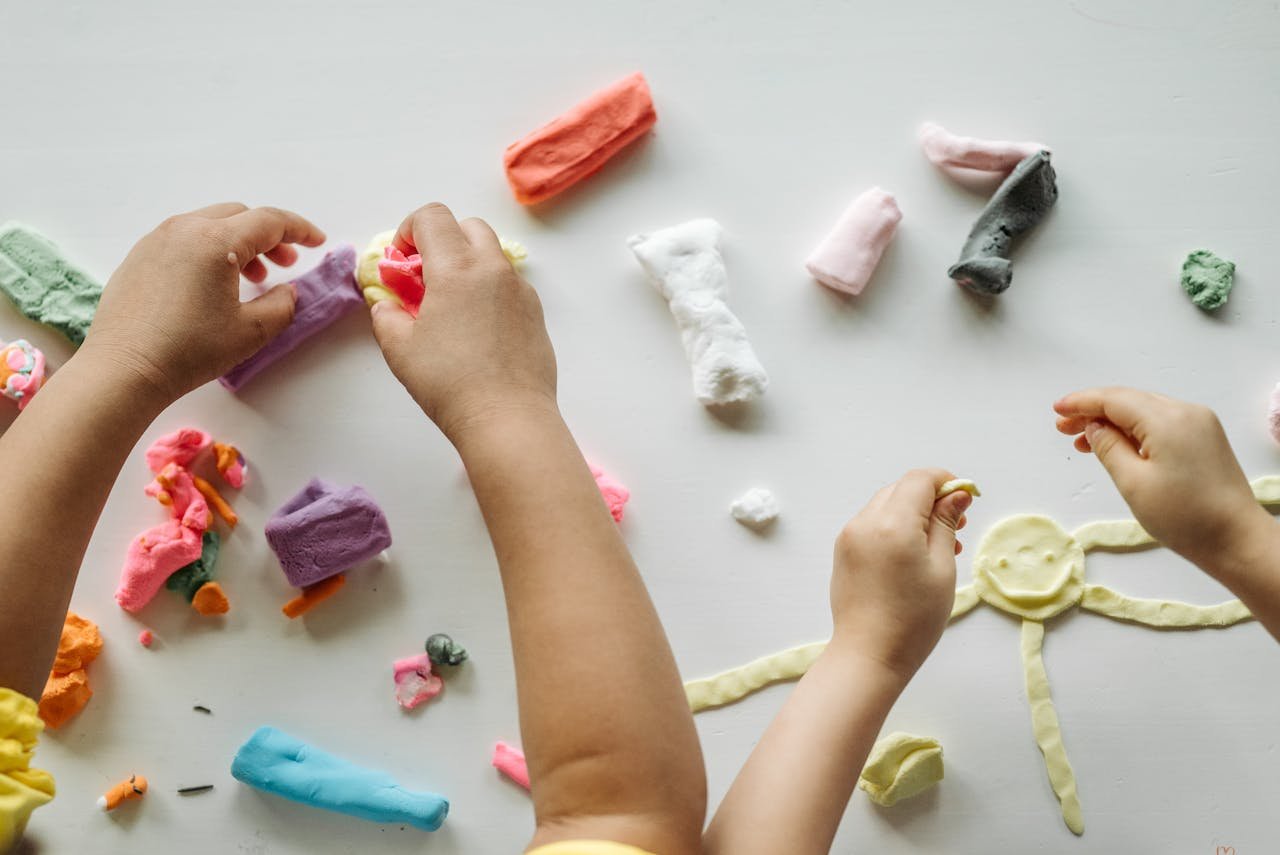 Services-02 Children engaged in creative clay play, forming shapes and exploring colors on a white table.