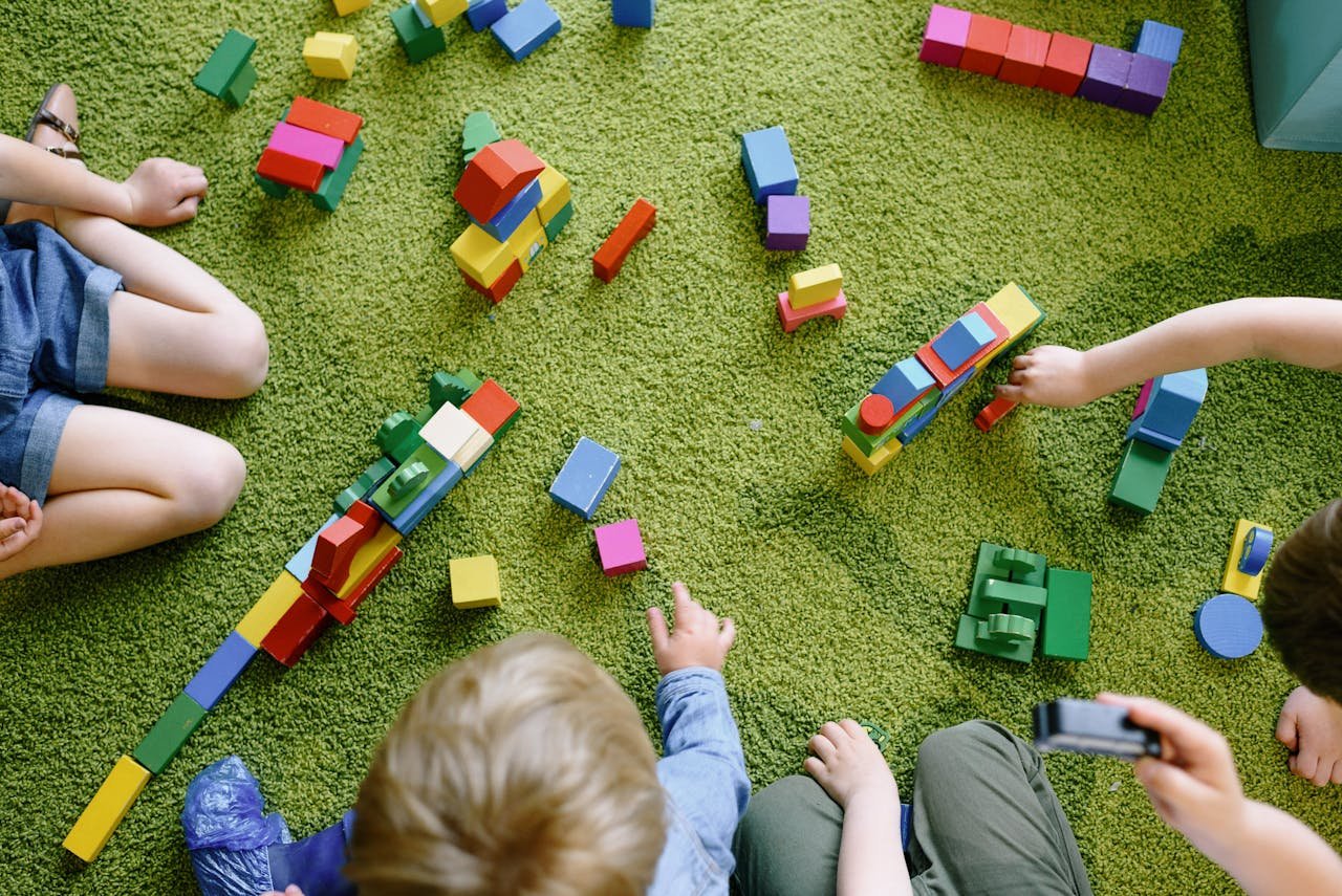 Services-01 Children playing with wooden blocks on a green carpet in a classroom setting.